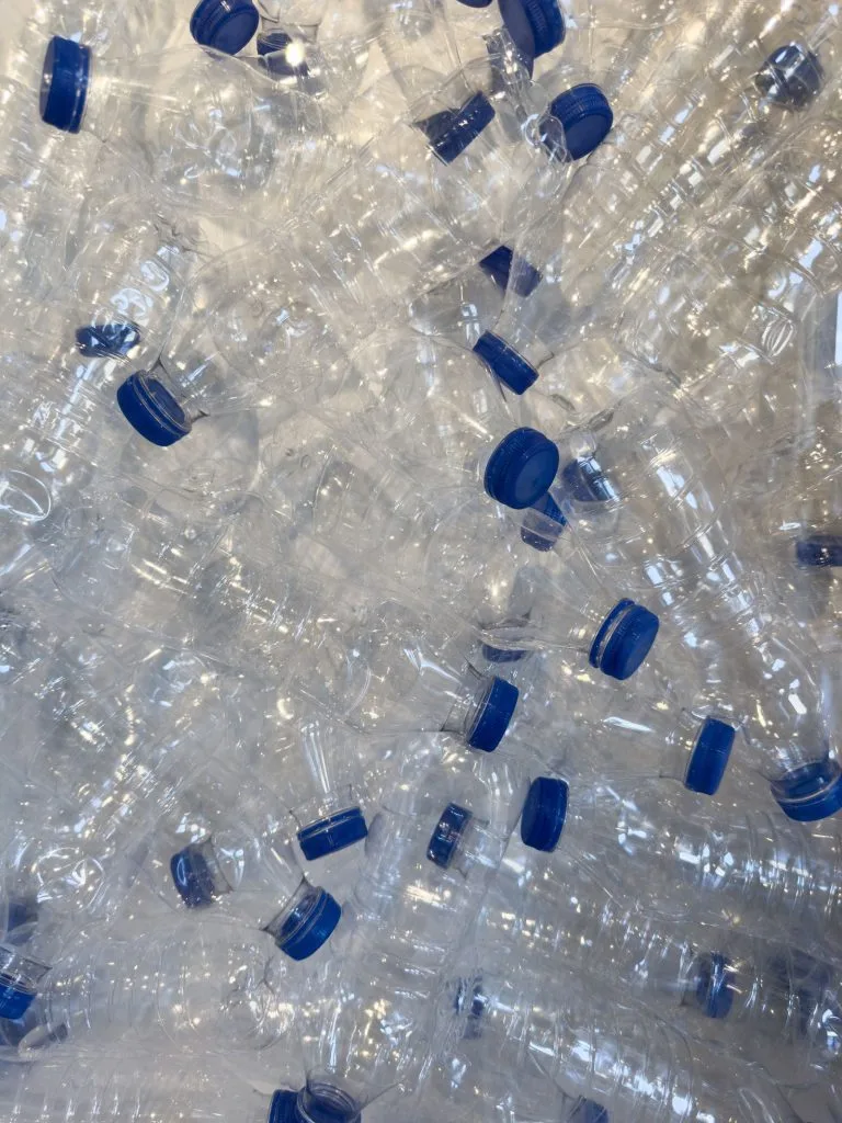 Clear PET bottles with blue caps piled together as feedstock for food grade recycled PET