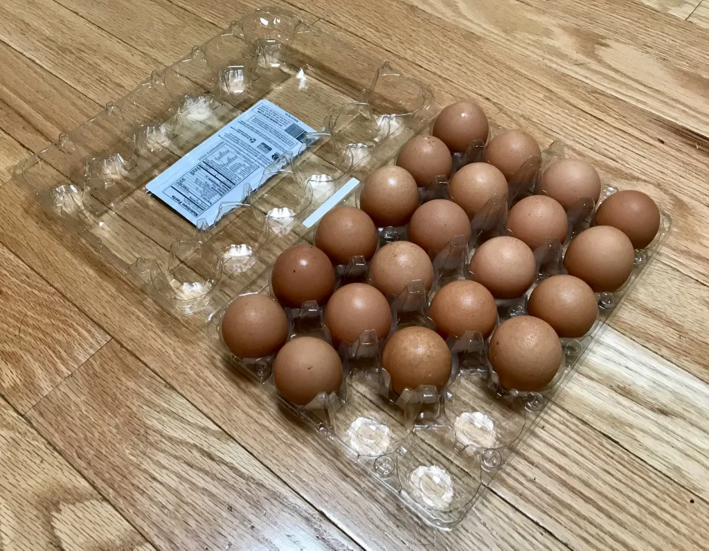 Clear hinged plastic egg carton with brown eggs and a printed label panel inside the lid